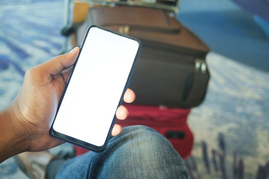Viajero revisa la app de su aerolínea en el celular para acumular millas volando desde el aeropuerto