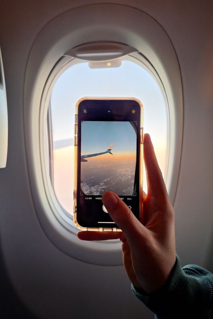 Pasajero con smartphone en la ventanilla del avión tras convertir puntos AMEX a DOTERS